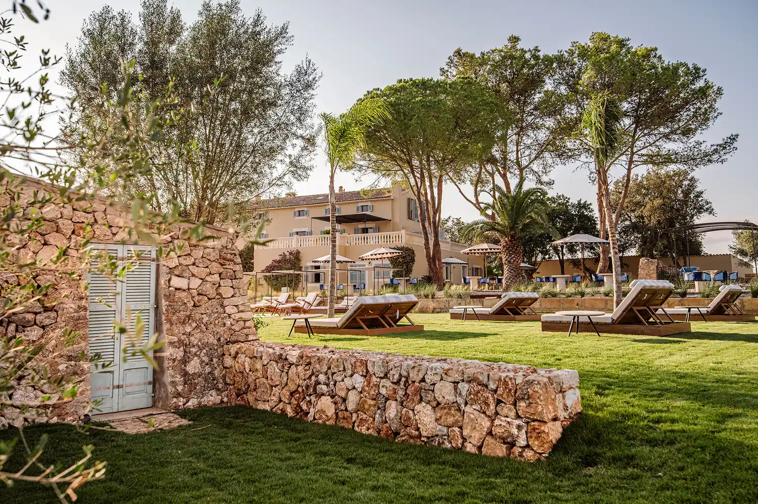 Sun loungers and day beds arranged on the hotel grounds beside a rustic stone wall.