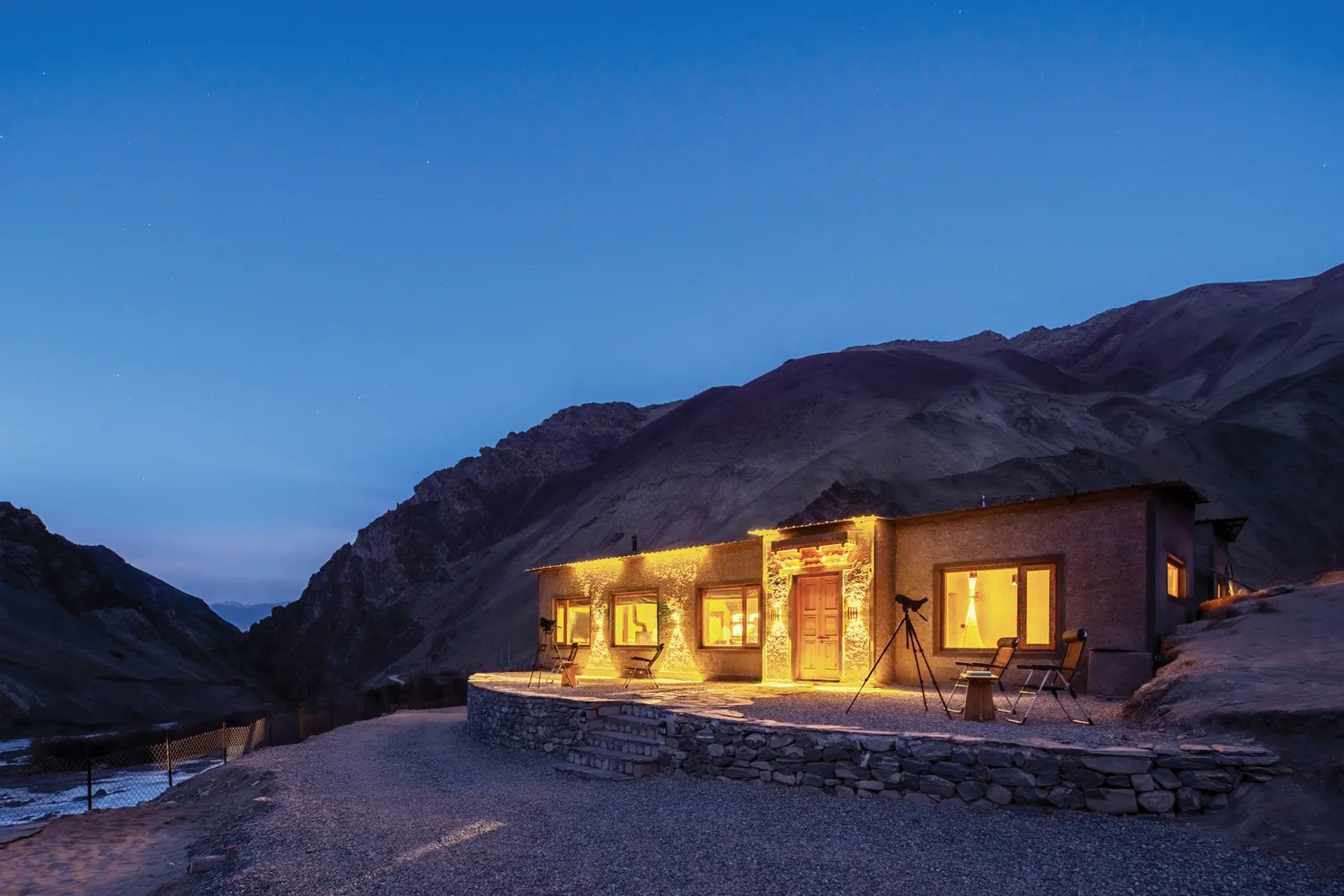A luxury mountain lodge illuminated at night against a backdrop of jagged mountain peaks.