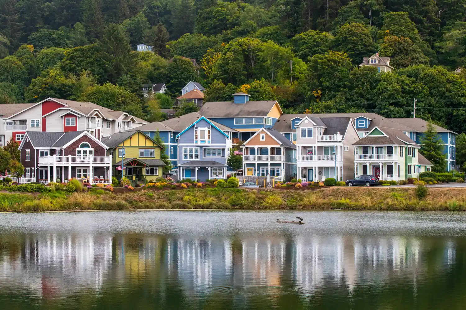 Technicolor houses on stilts along a quiet riverfront under a overcast sky in the Pacific Northwest.