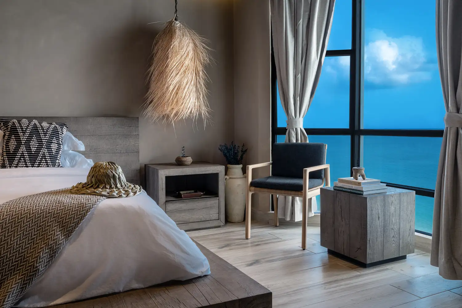 A hotel bedroom with a large window offering a clear view of the turquoise ocean water.
