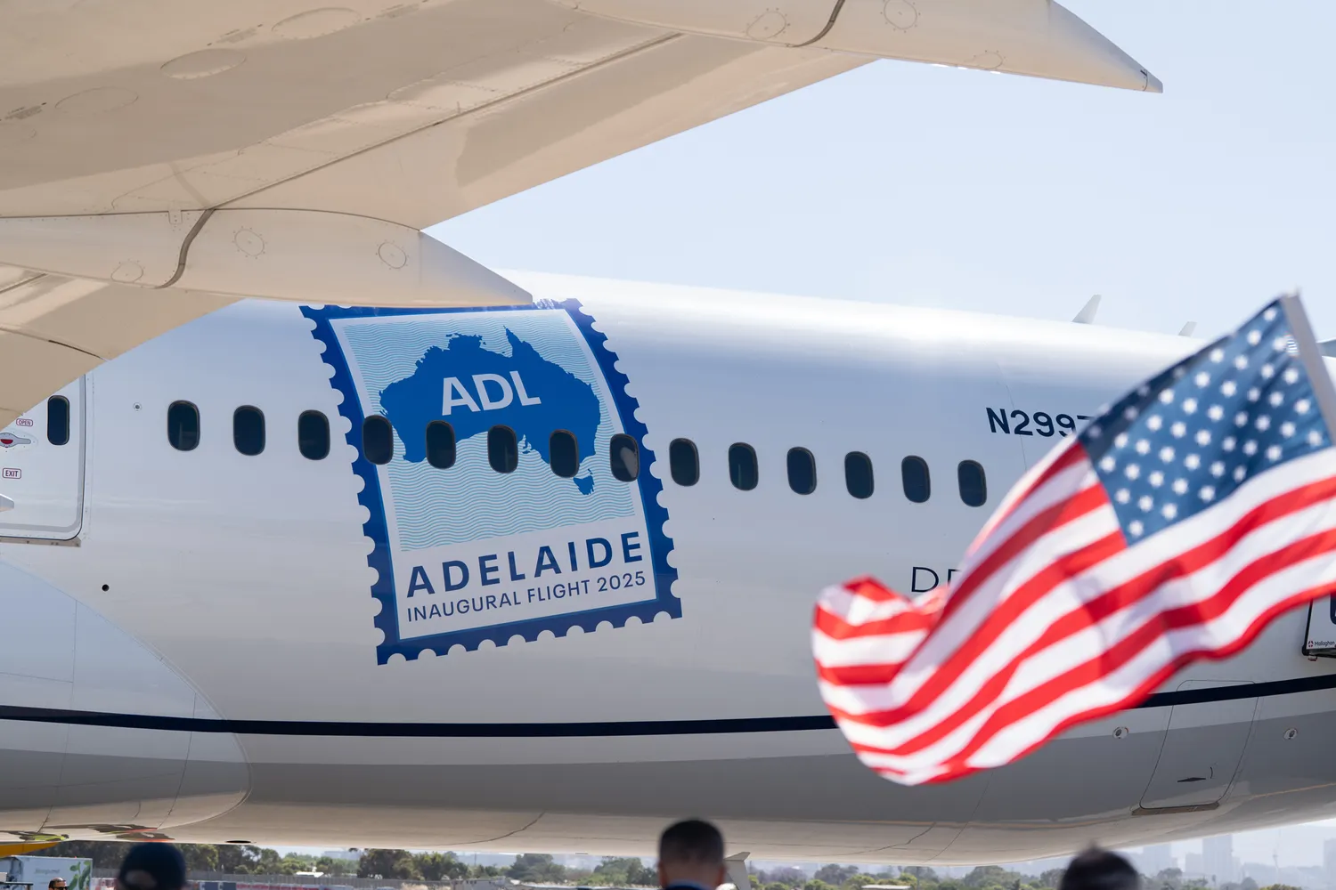 A United Airlines airplane on the tarmac in Adelaide featuring an inaugural flight decal and a US flag.