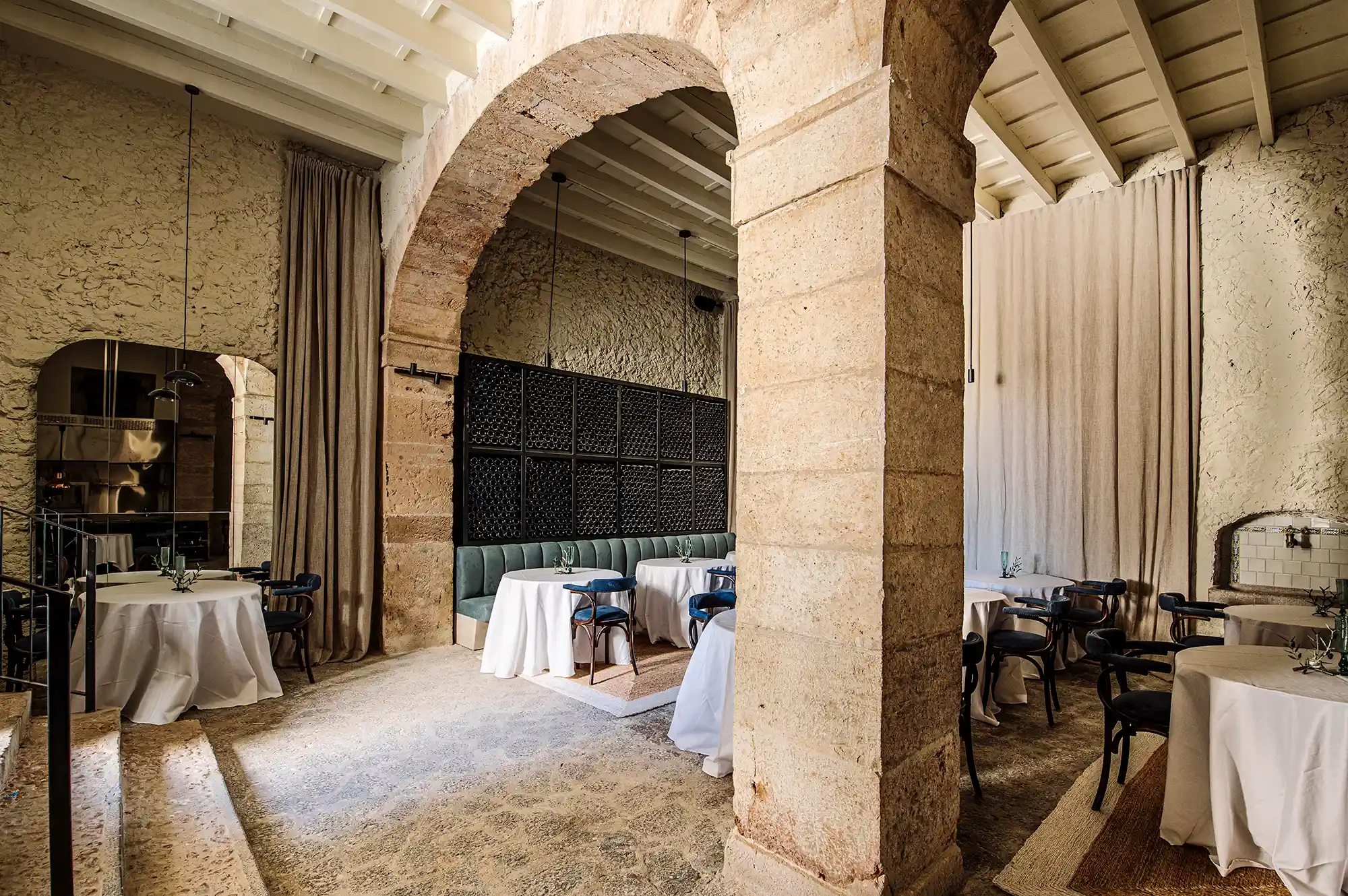 An indoor dining area featuring historic stone arches and tables with white tablecloths.