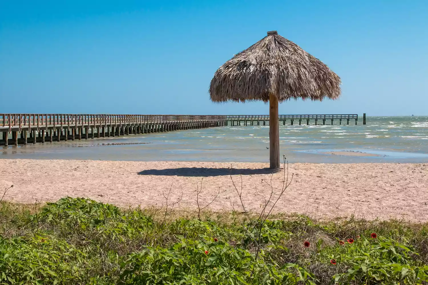 A wooden fishing pier extending into the calm Gulf waters at Rockport Beach, Texas.