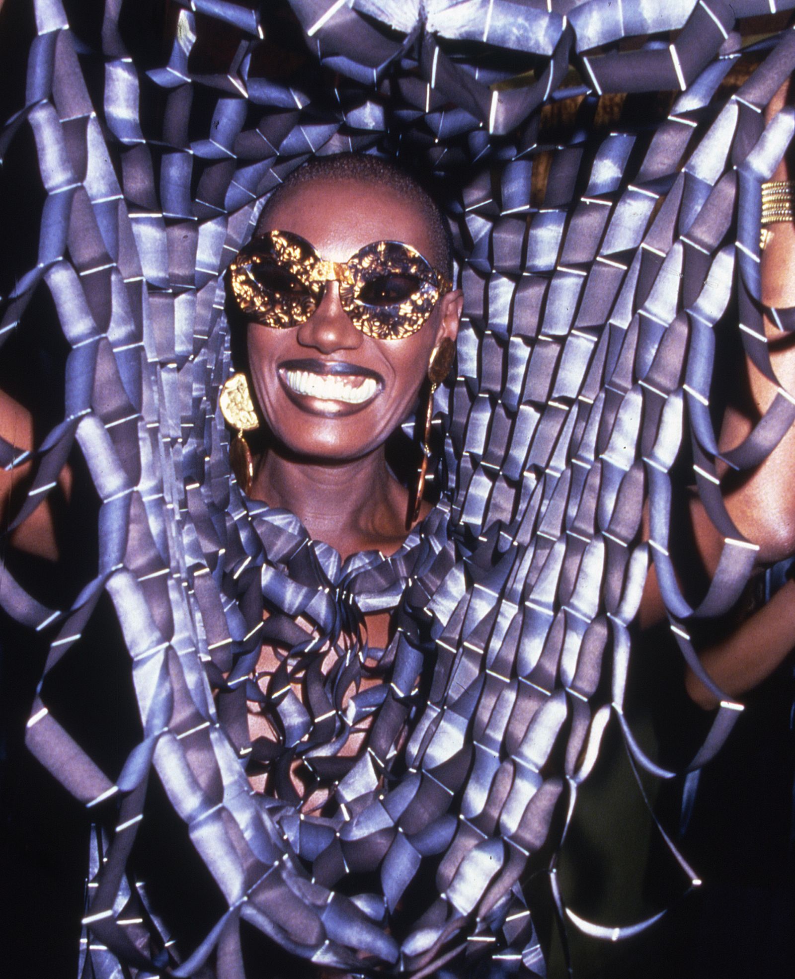 Close-up portrait of a person in high-fashion sunglasses and vibrant accessories.