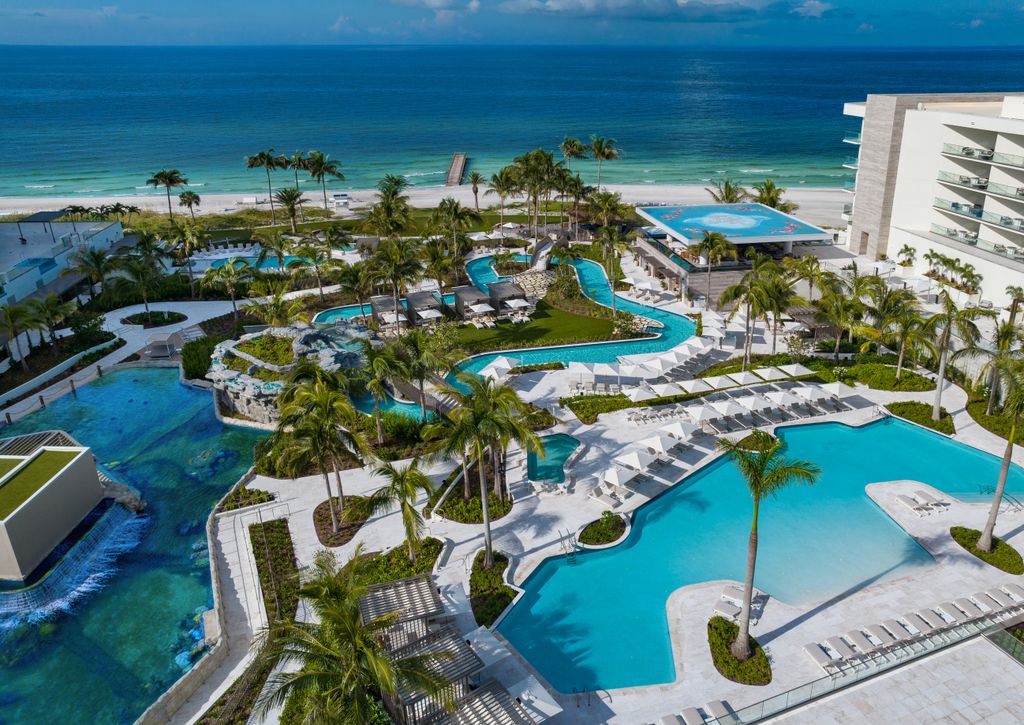 A luxury resort pool area with neutral-toned architecture and lush tropical plants overlooking the sea.