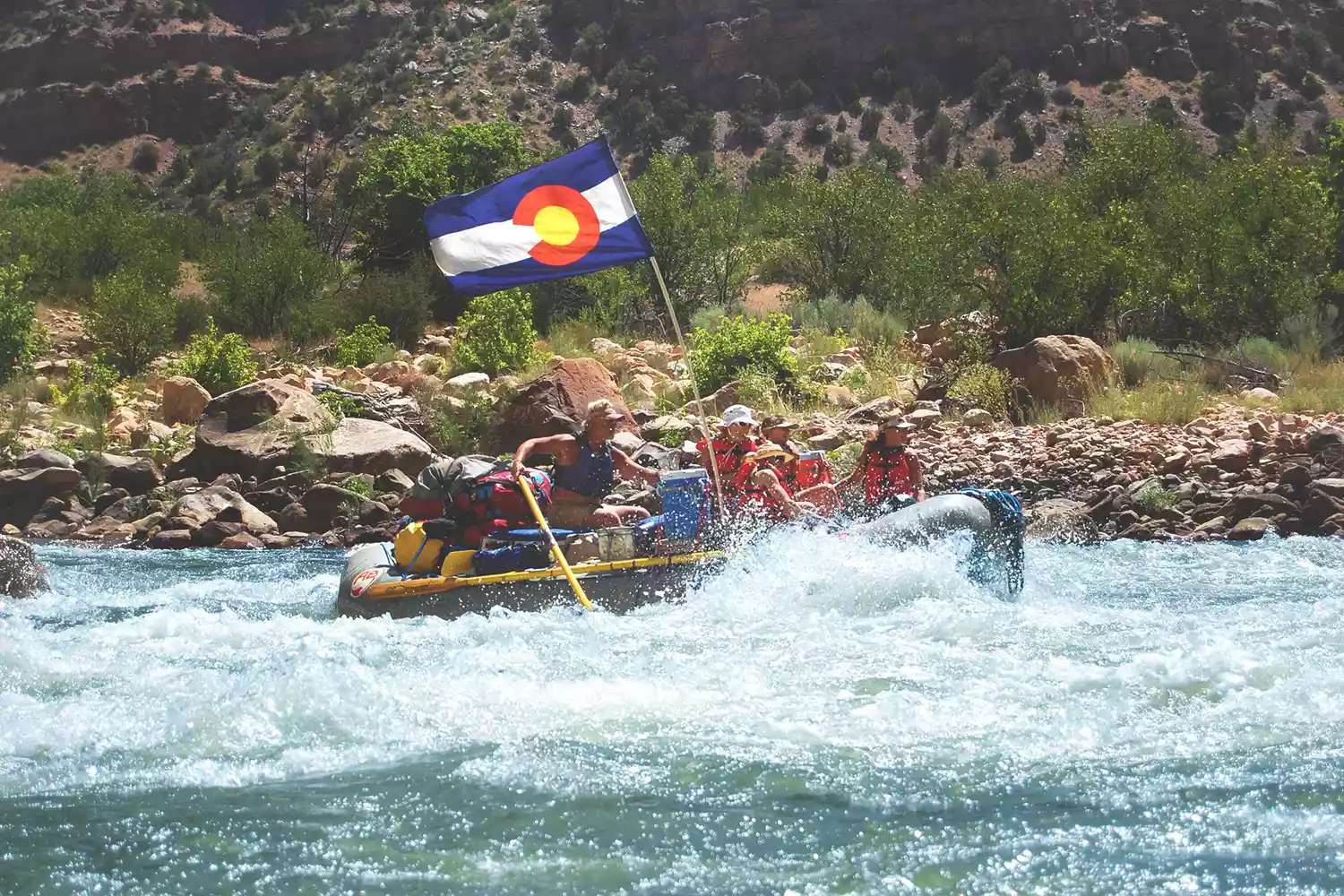 A group of people in a large raft navigating a calm, scenic stretch of the Colorado River in Ruby-Horsethief Canyon.