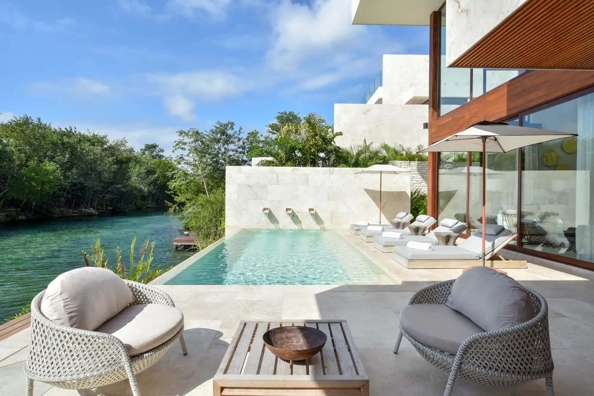 An outdoor lounge area and pool overlooking a quiet waterway at Rosewood Mayakoba.