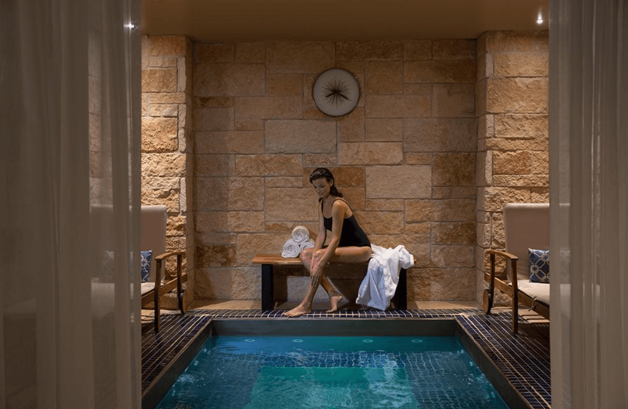 A guest relaxing at the edge of a serene indoor swimming pool.