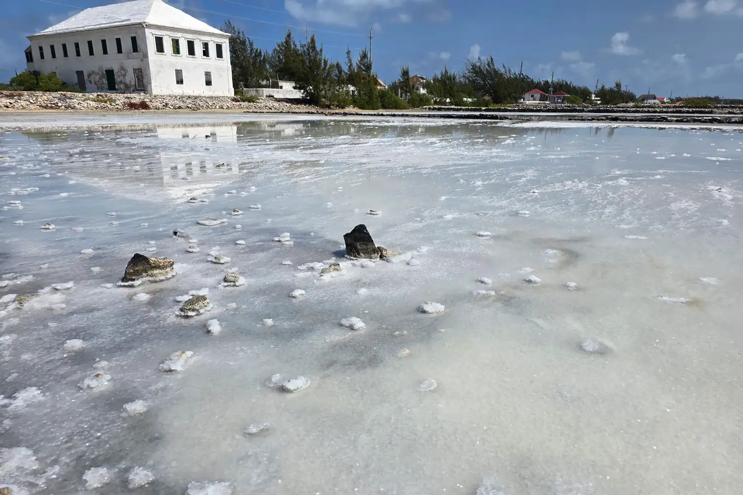 Salt pans and rock formations on Salt Cay with a historic white building in the background.