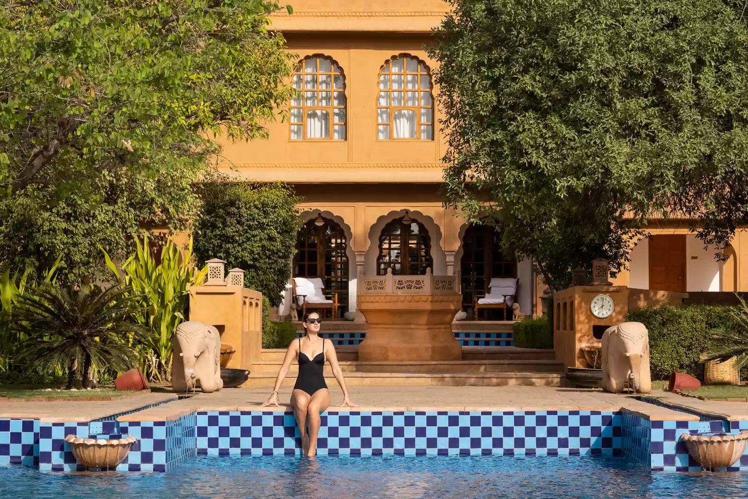 A guest relaxing in a sun lounger by a pristine swimming pool at The Oberoi Rajvilas in Jaipur.