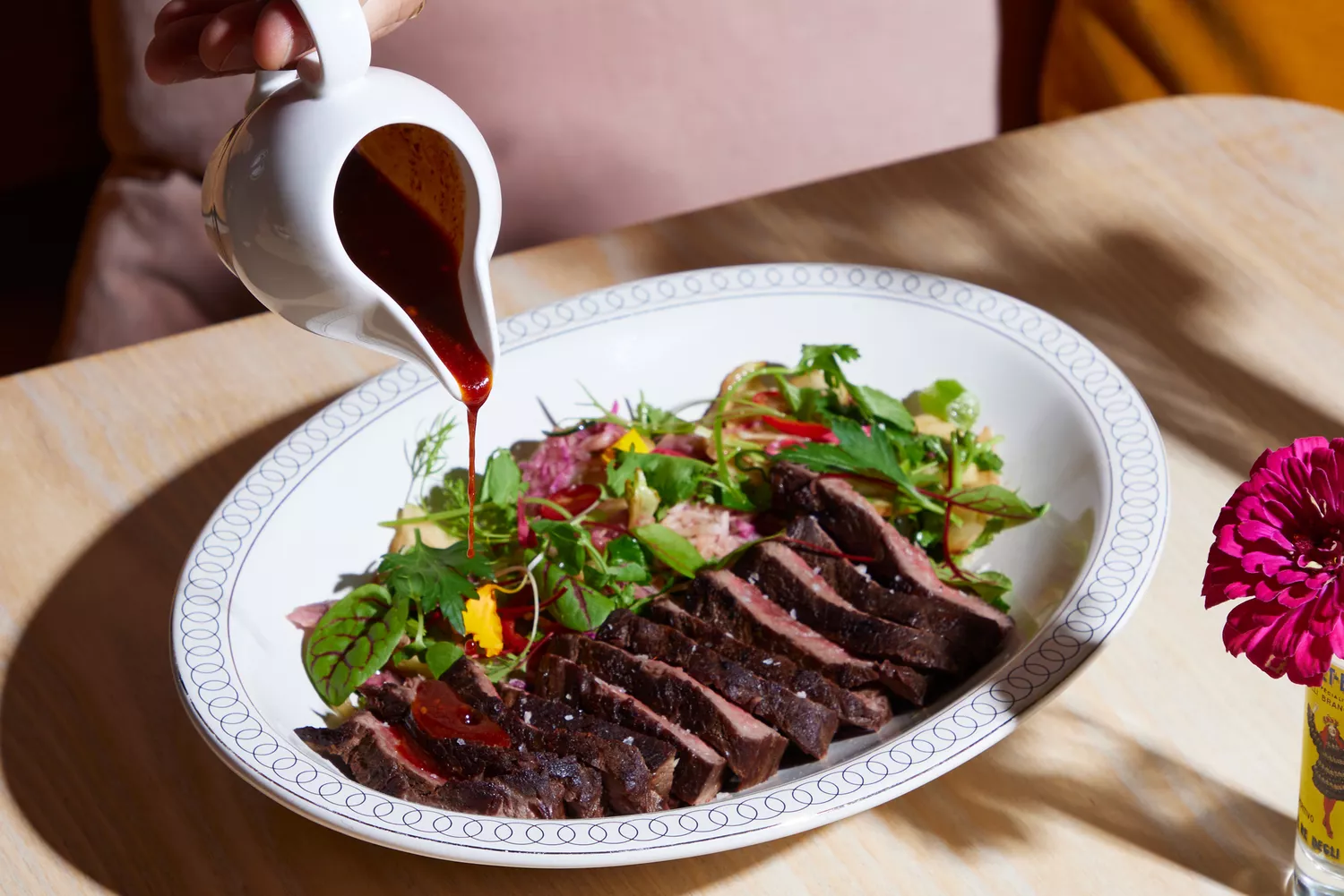 A chef pouring dressing over a steak and salad plate at Little Bear.