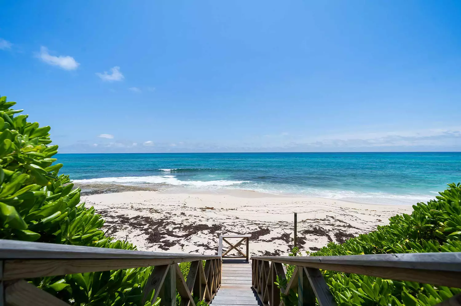 A sandy path lined with lush tropical greenery leading toward a bright white sand beach.