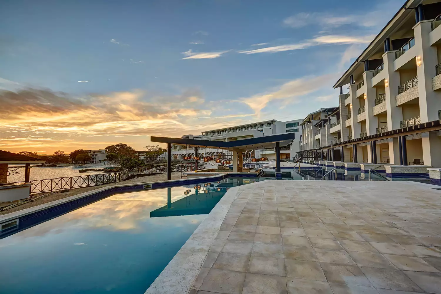 The pool deck at Hideaway at Royalton Negril during a vibrant orange and purple sunset.