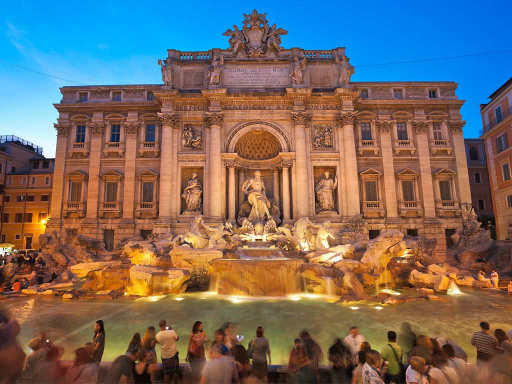 The Baroque facade and water basin of the Trevi Fountain with tourists around the edges.
