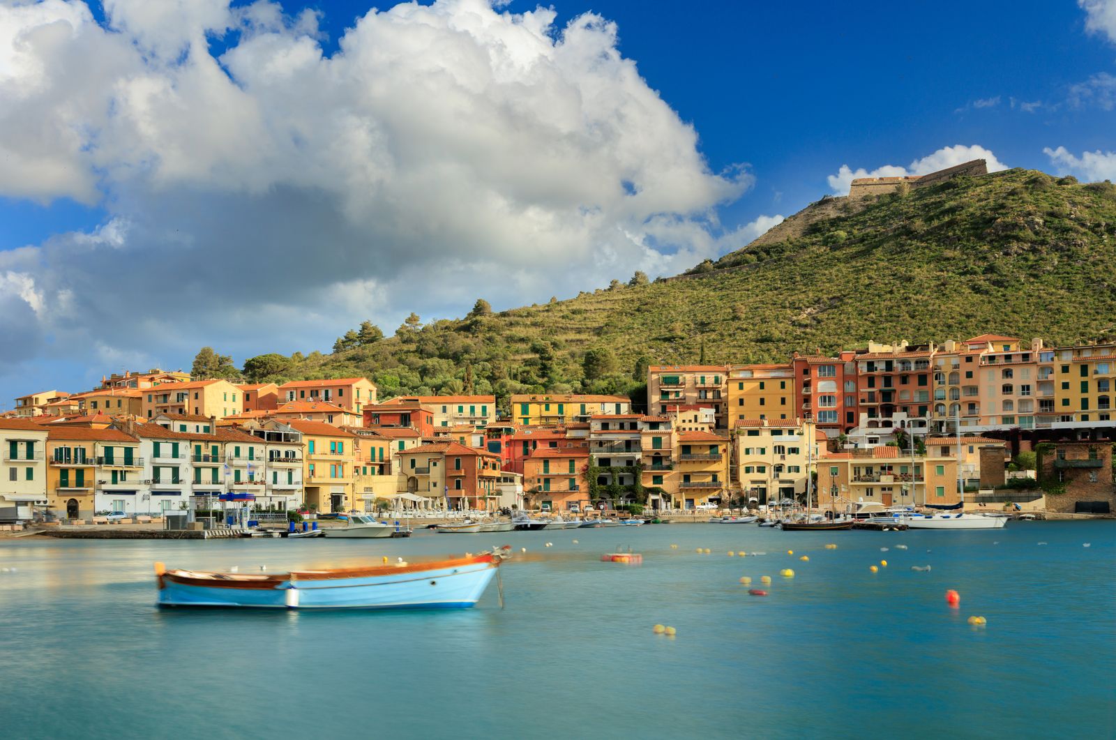 A boat traveling through the sea near a colorful Italian coastal landmark.