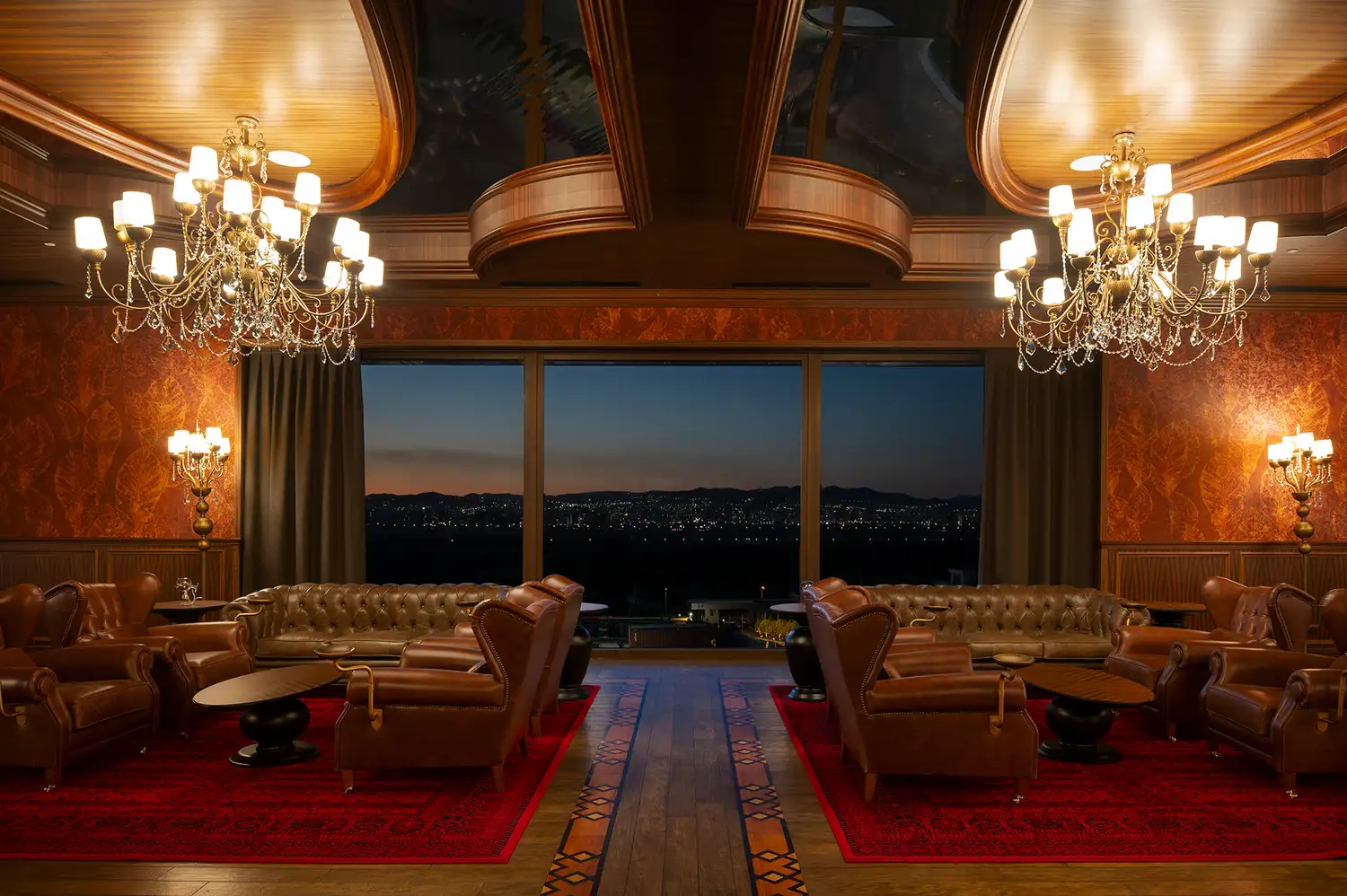 A luxurious lounge with leather seating and large windows overlooking the city lights at dusk.