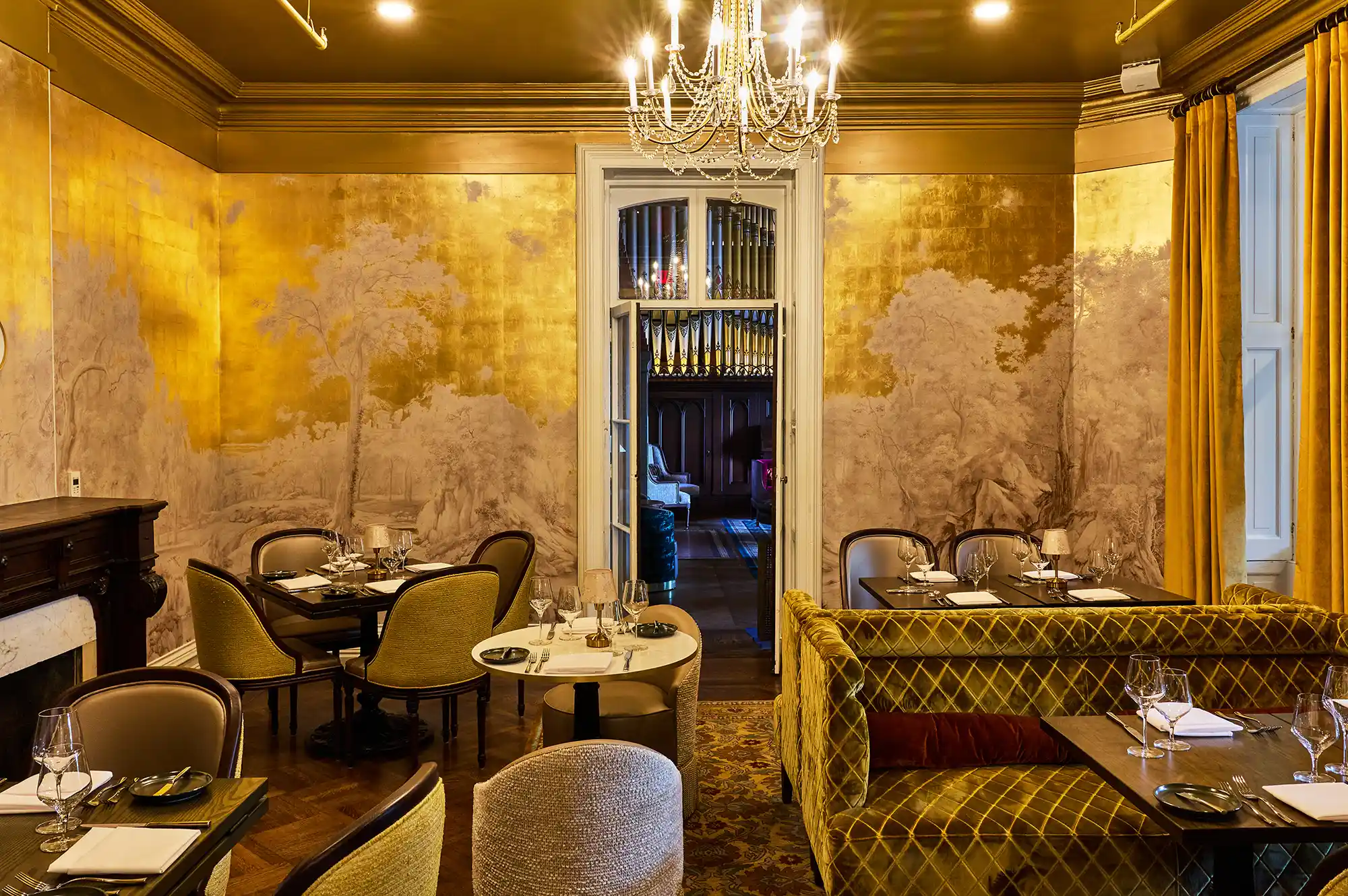 A luxurious dining room with muralled walls, white tablecloths, and a crystal chandelier.
