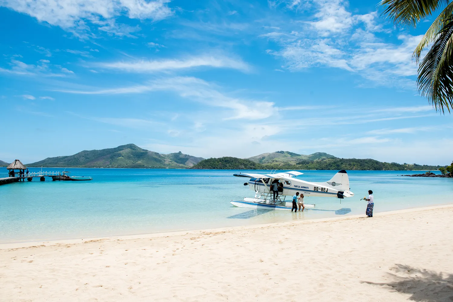 A yellow and white seaplane anchored in the shallow blue water near the shore of Turtle Island.