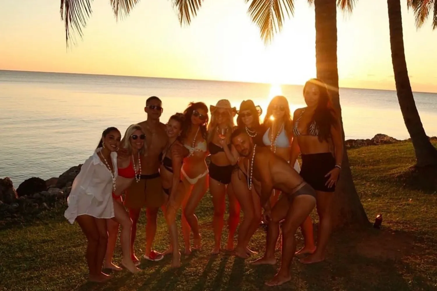 A group of friends posing together by the water during a sunset in Fiji.