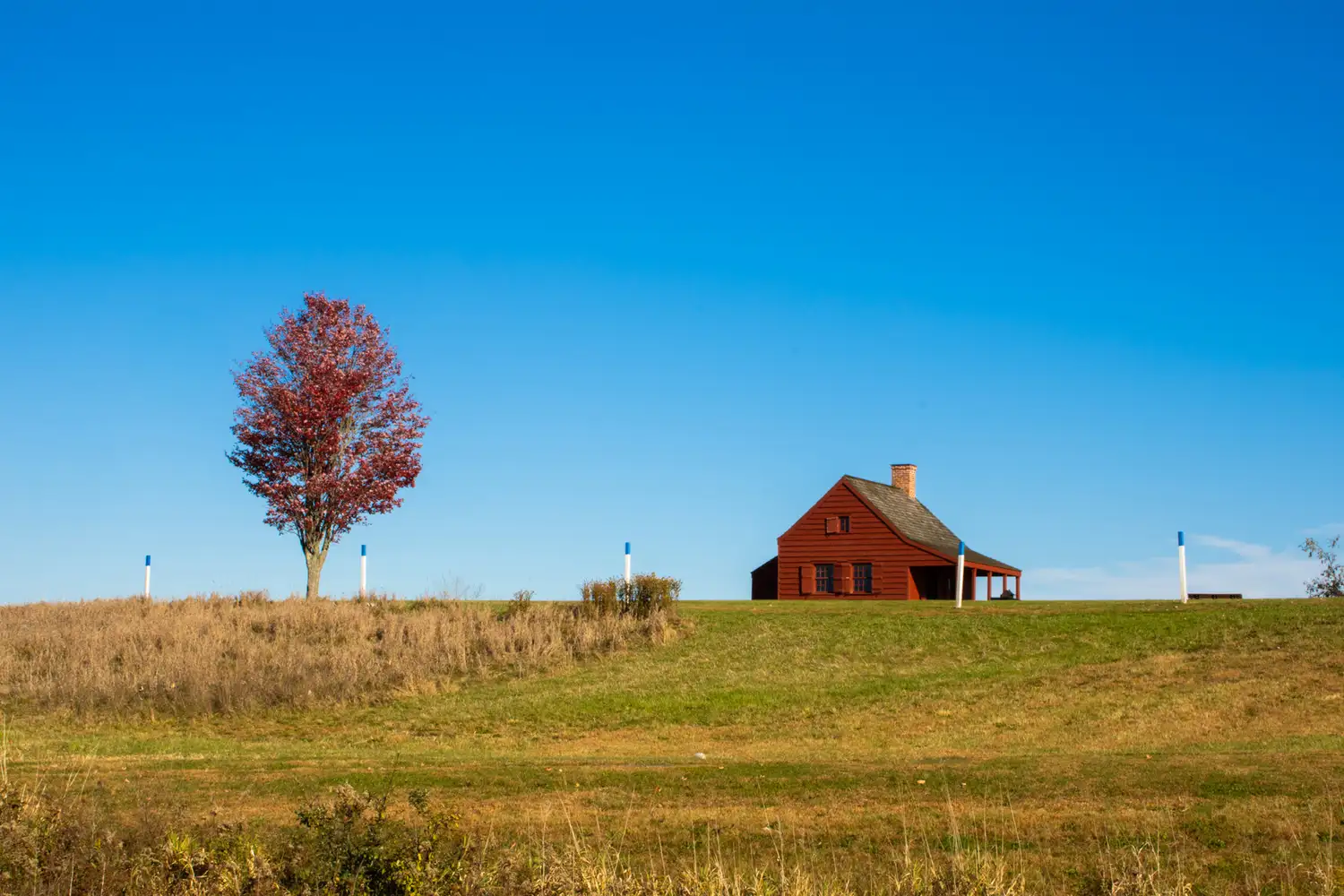A historic red wooden building on a grassy field at Saratoga National Historic Park.