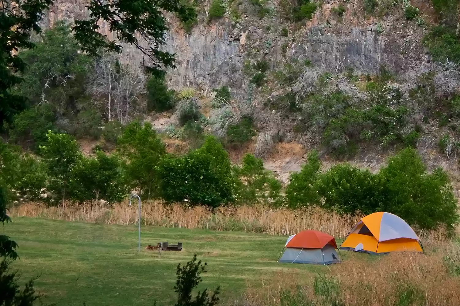 Two camping tents pitched on a rocky cliffside overlooking a valley in Colorado Bend State Park.