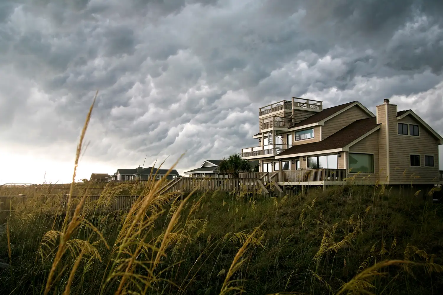 A multistory beachfront house on Fripp Island under a cloudy sky with beach grass in the foreground.