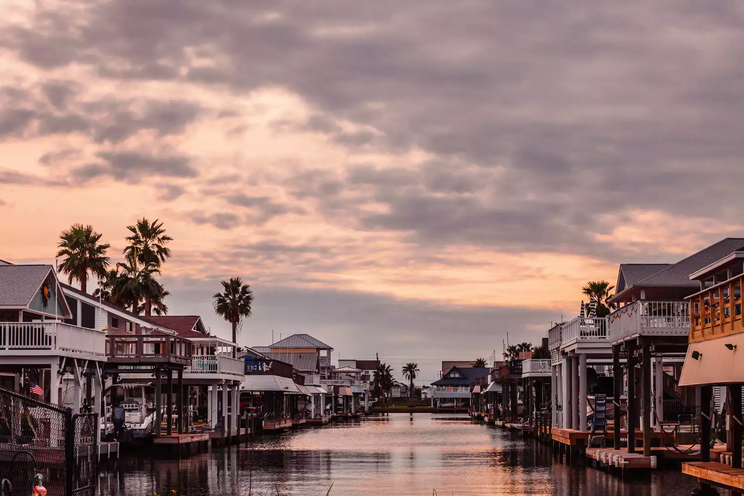 Waterfront vacation homes in Jamaica Beach, Galveston, during a vibrant pink and orange sunset.