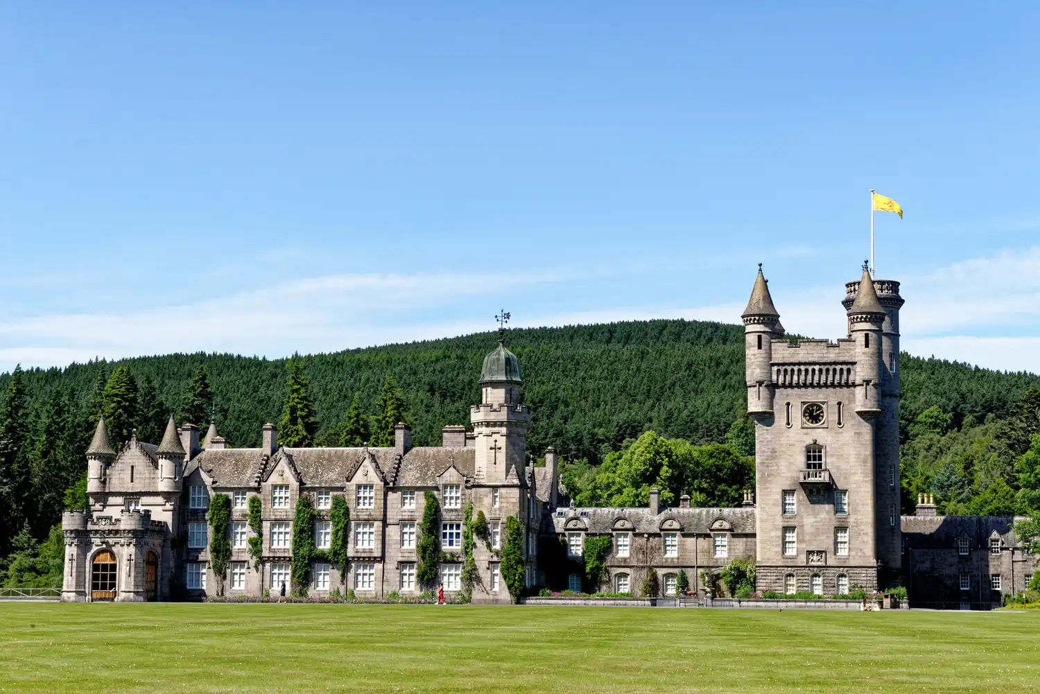 A sunny day view of Balmoral Castle surrounded by lush green forests.