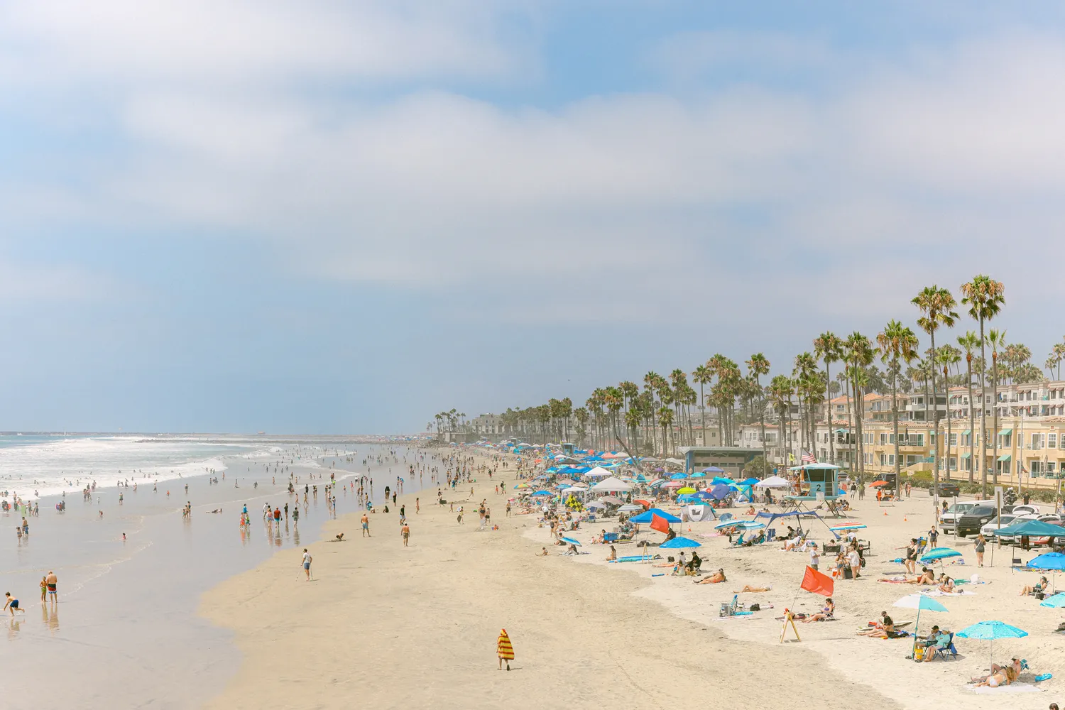 A crowded, sunny beach in Carlsbad with numerous beachgoers and colorful umbrellas.