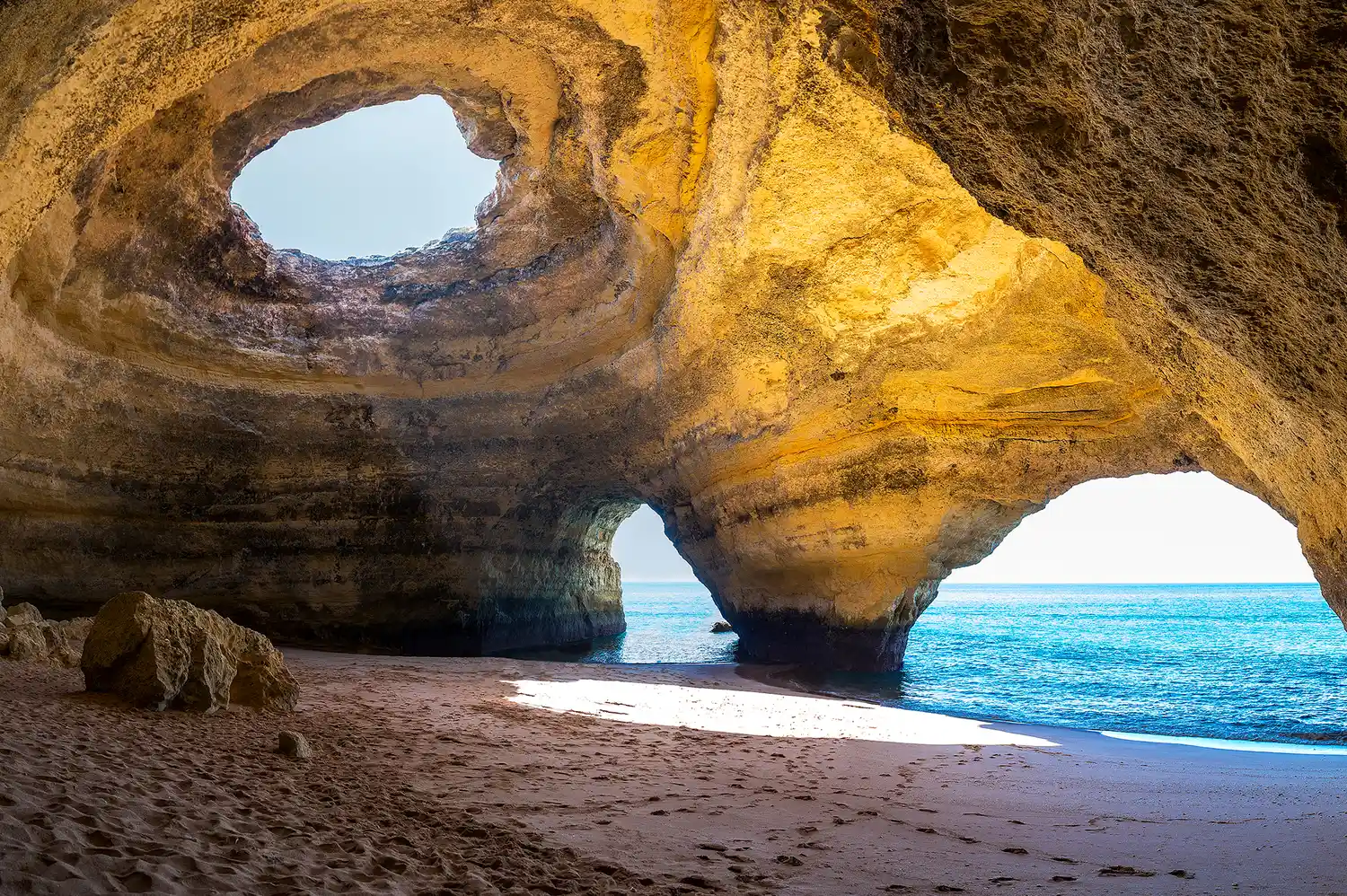 Inside the Benagil Cave looking up through the opening at the sky with the beach inside.