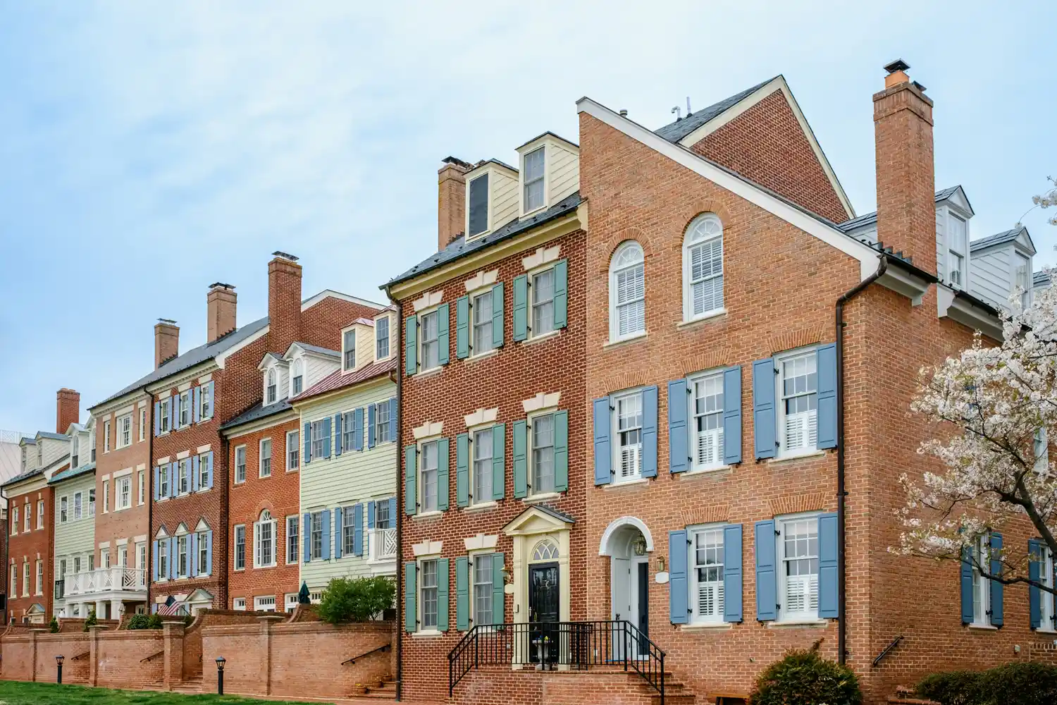 A row of historic brick townhouses with shutters along a sidewalk in Old Town Alexandria.