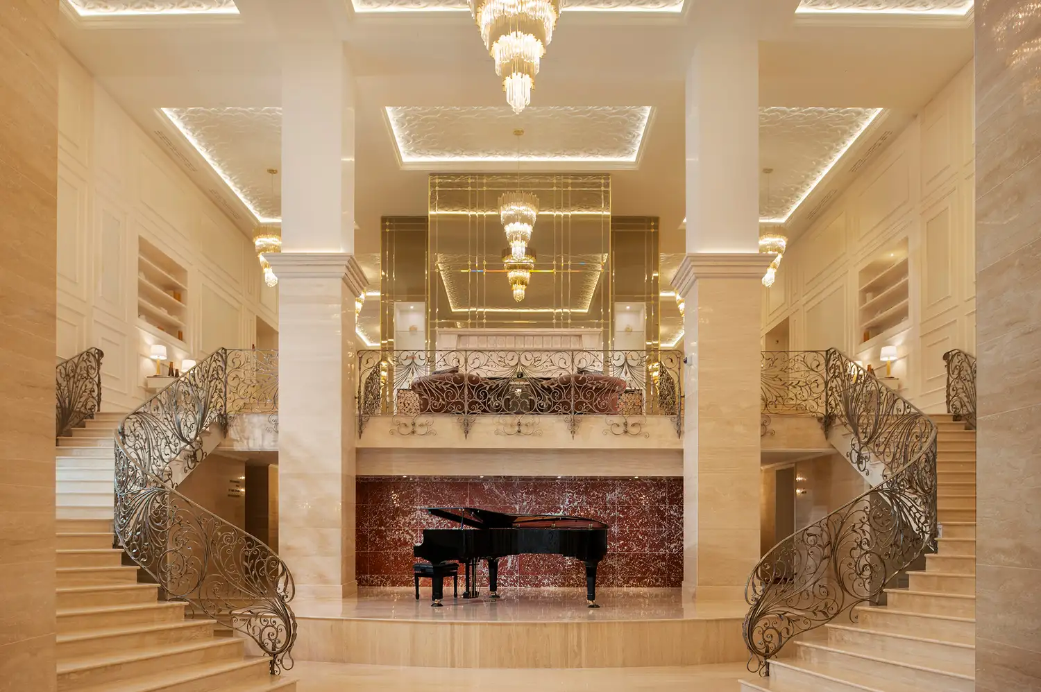 The grand hotel lobby featuring a central piano, a curved staircase, and high-end finishes.