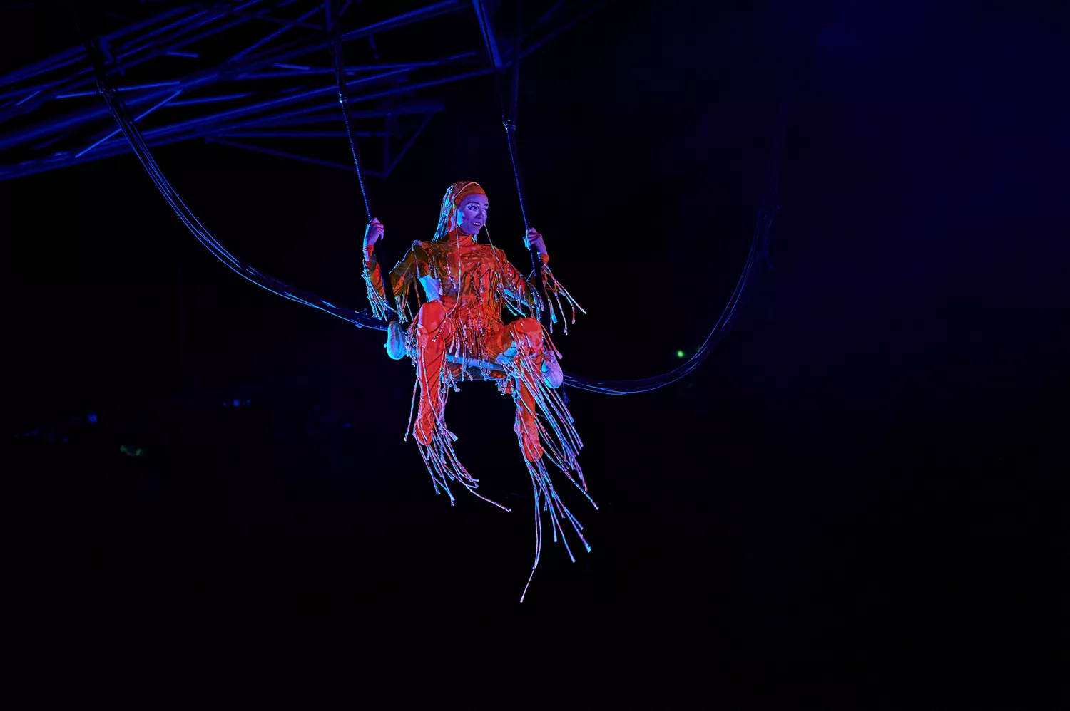 A performer in a vibrant bungee costume suspended during a Cirque du Soleil Mystère performance.