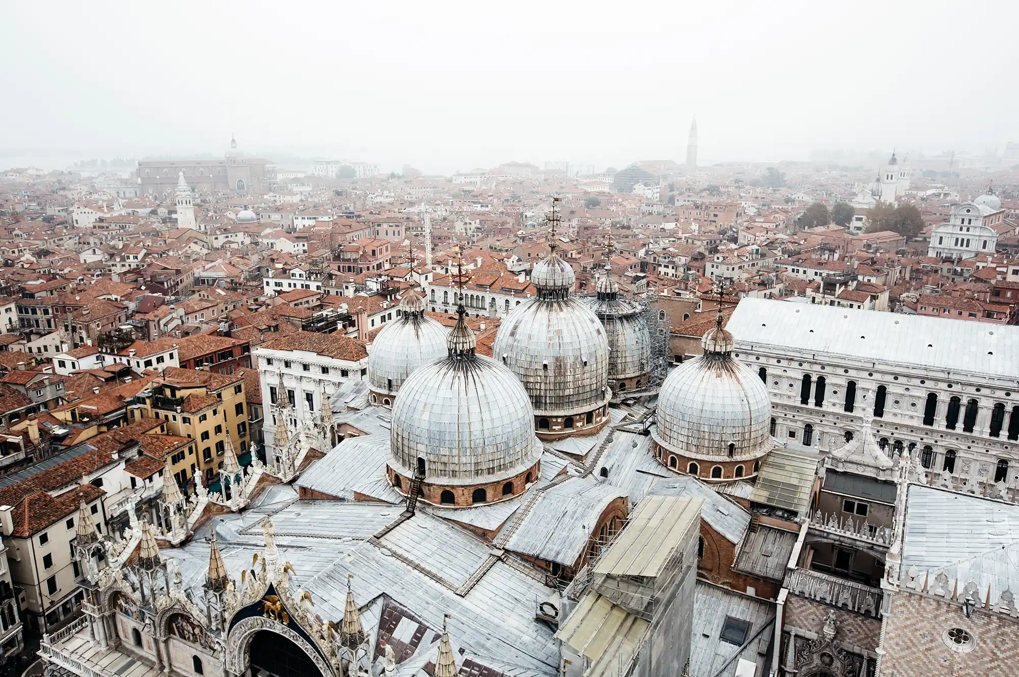 Aerial view of St. Mark's Basilica in Venice shrouded in a thick winter mist with surrounding red rooftops.