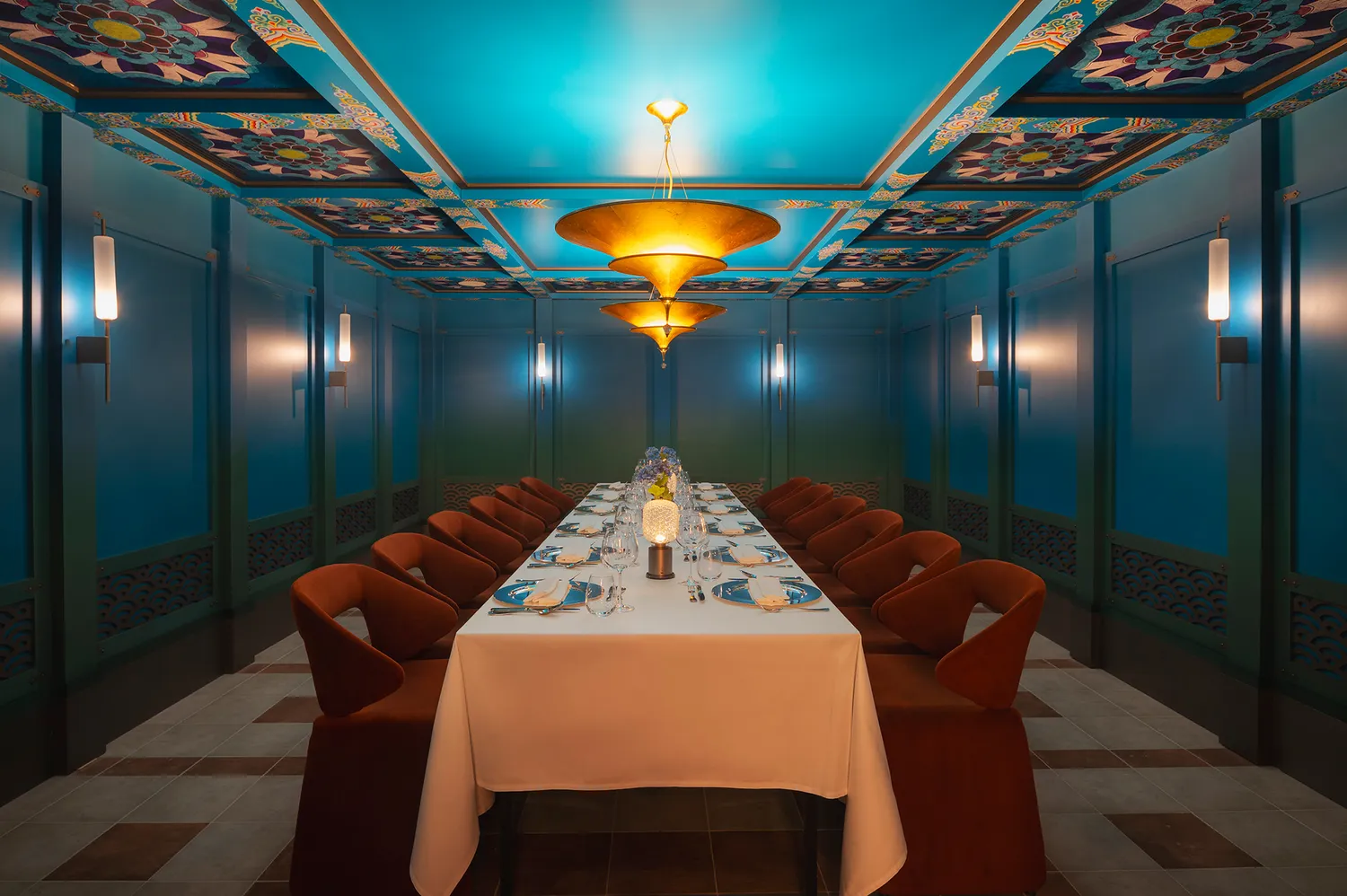 An ornate dining room with blue decorative walls and a long table set for a formal meal.