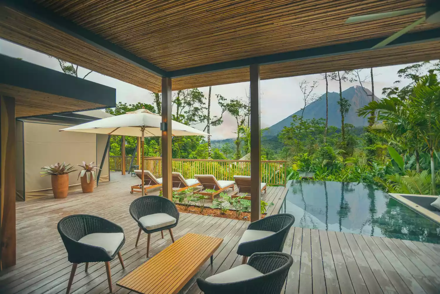 An infinity pool area at a luxury resort with a clear view of the cone-shaped Arenal Volcano in the background.