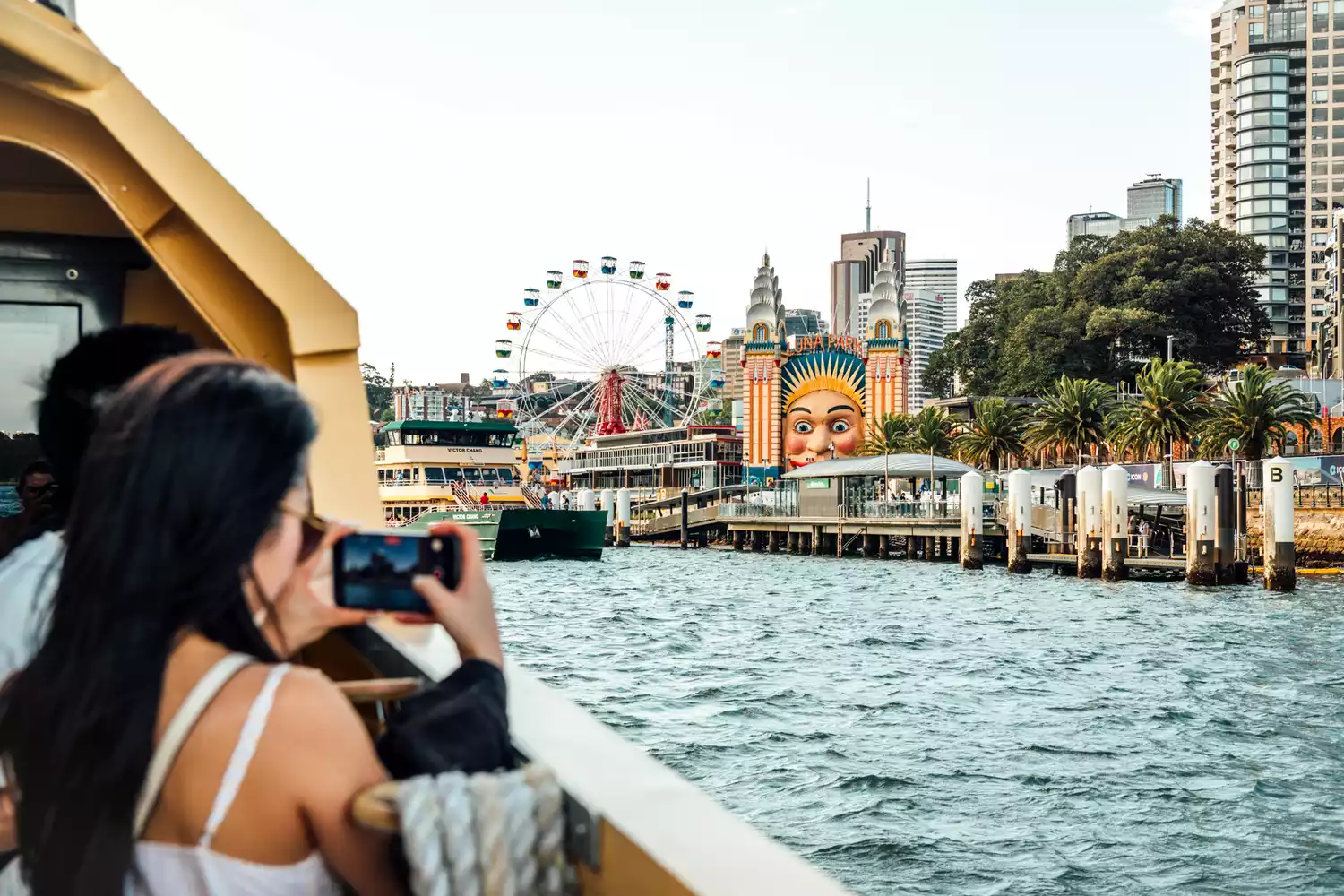 A person taking a picture of the Sydney skyline from a ferry on the water.