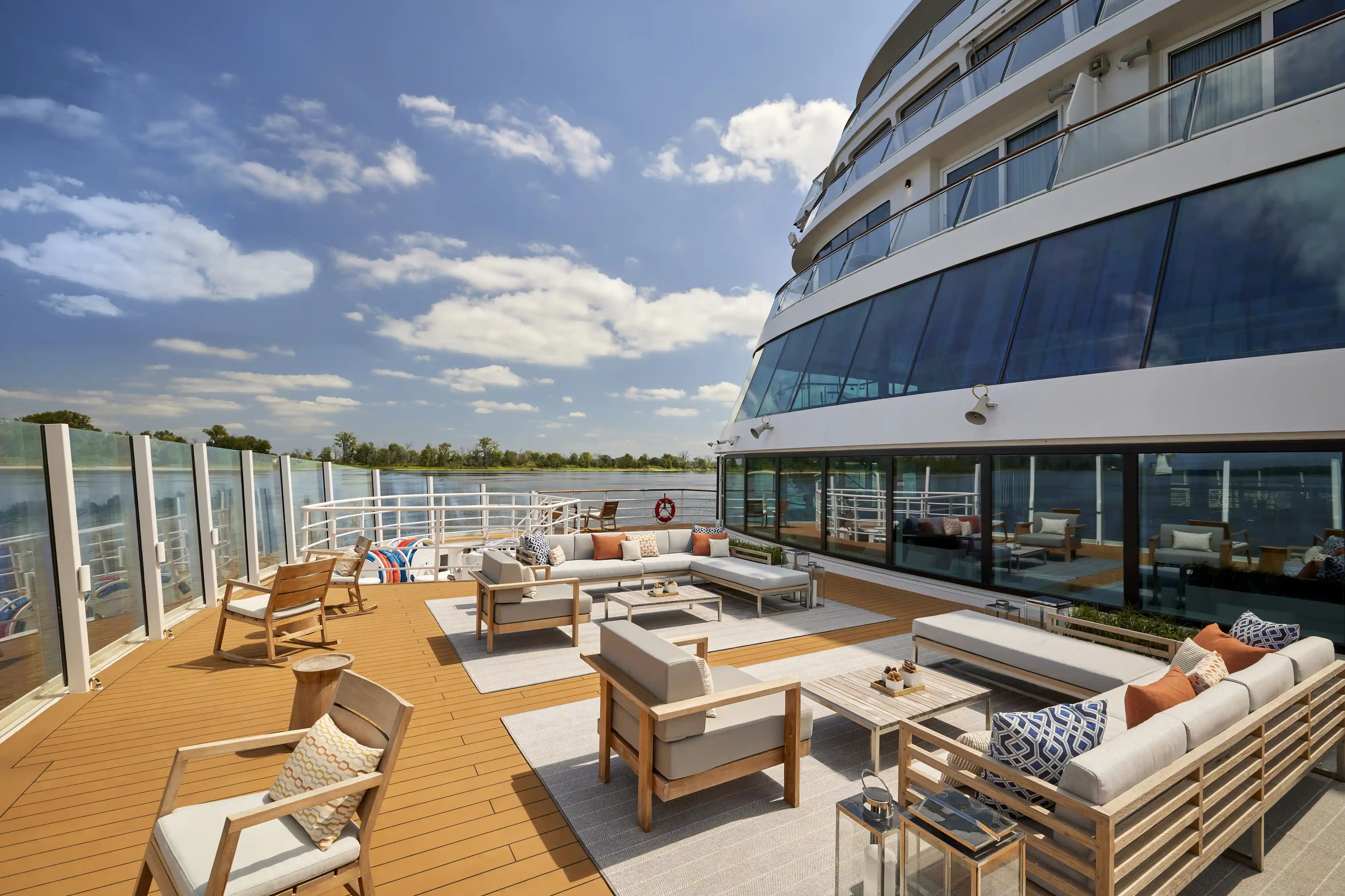 Outdoor wooden deck of a riverboat with comfortable seating looking out over the water.