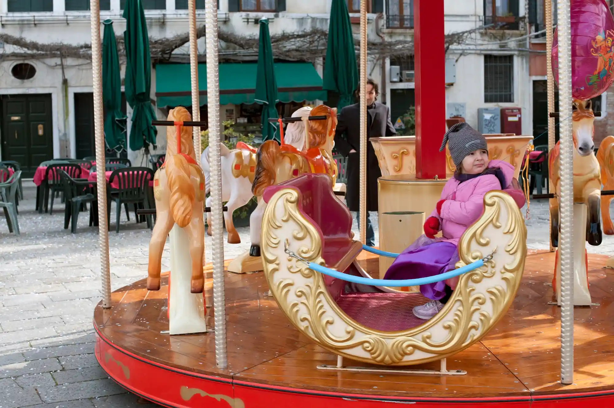A child enjoying a carousel ride in an outdoor Venetian square during the winter holidays.