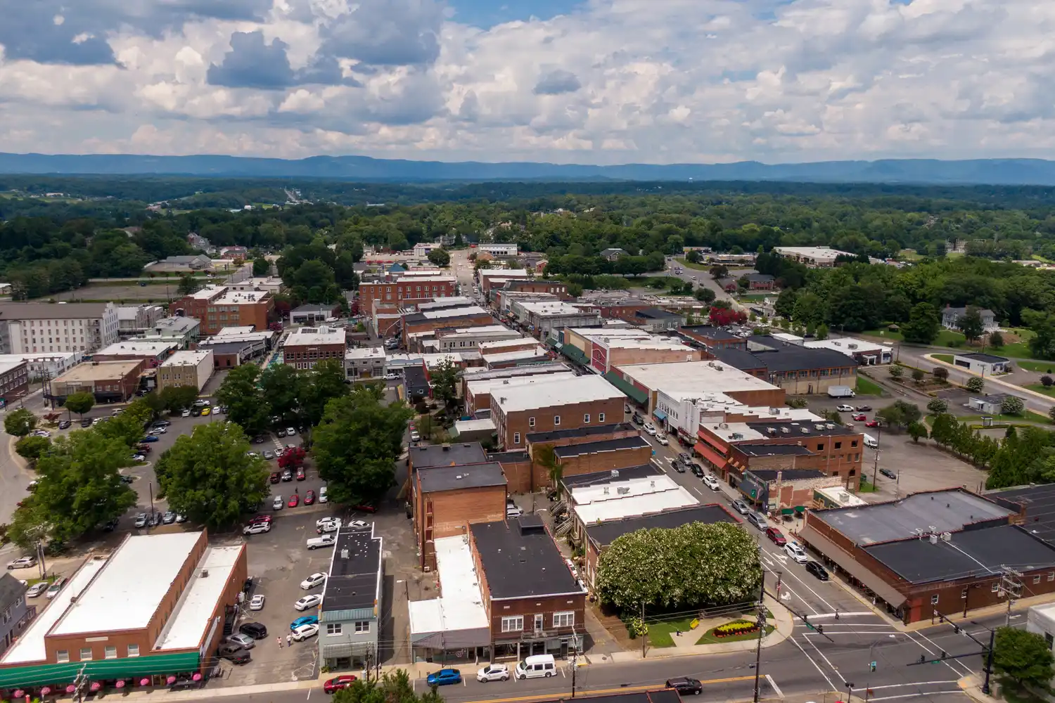 Aerial view of downtown Mount Airy surrounded by lush greenery and distant mountain peaks.