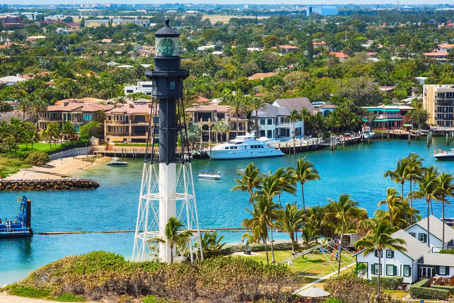 Aerial view of a lighthouse and waterfront residential properties with boats and palm trees in Pompano Beach, Florida.