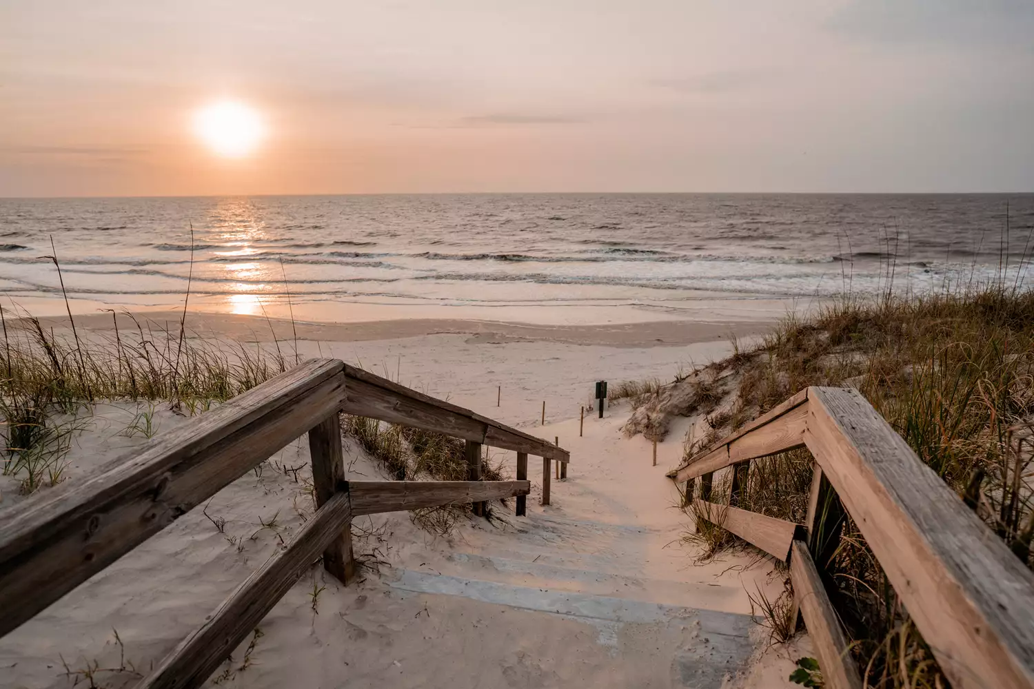 A wooden staircase leads over a dune to a Jekyll Island beach at sunset.
