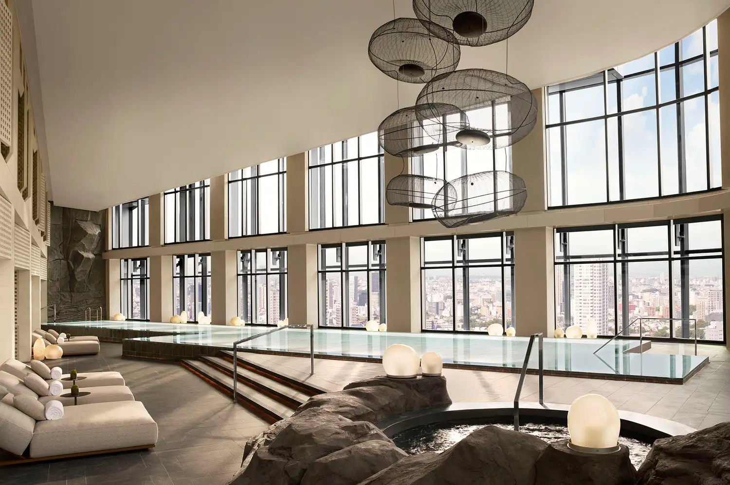 A 25-meter indoor heated swimming pool with lounge chairs and a view of the Tokyo skyline.