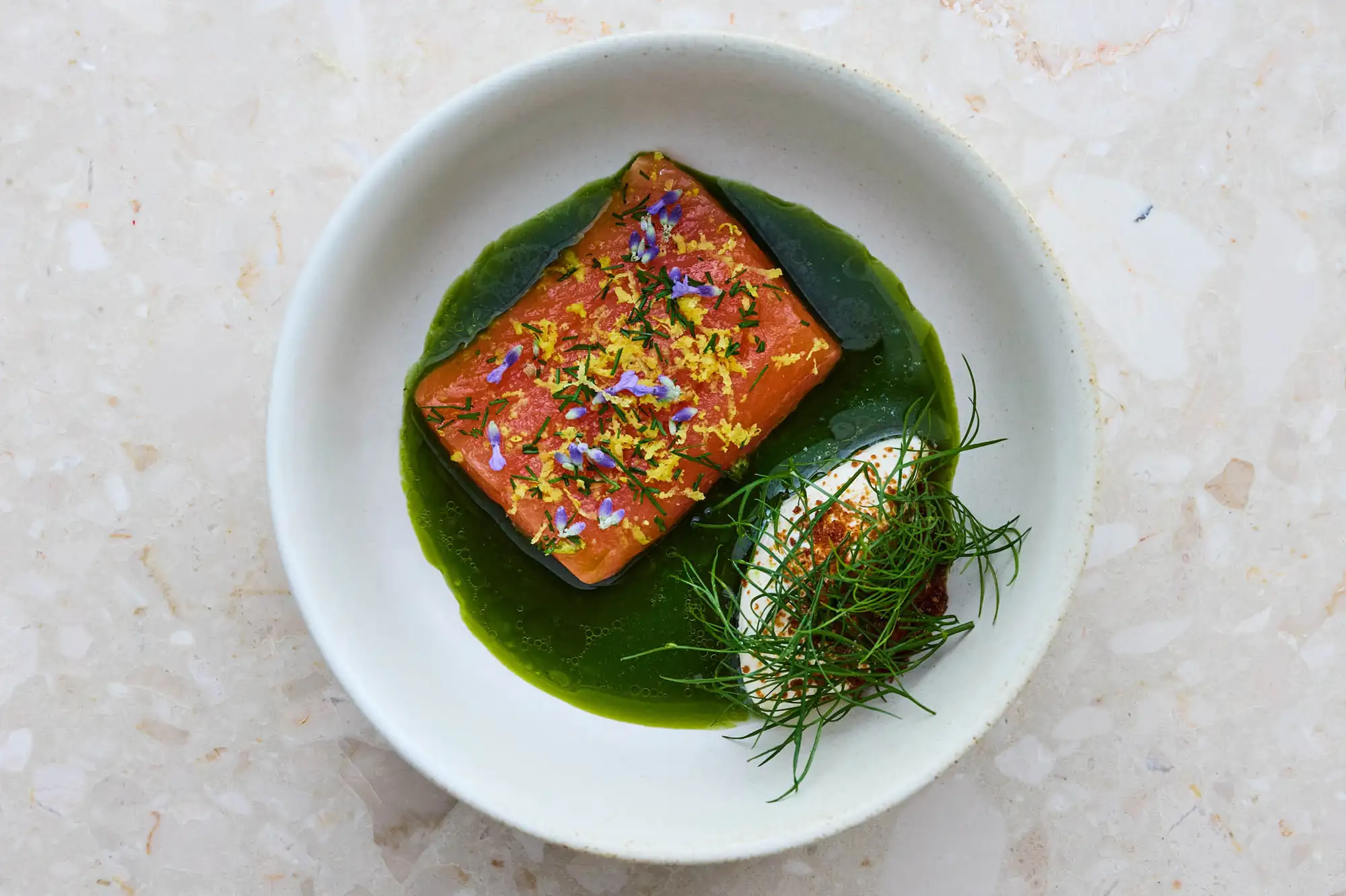 A gourmet plated dish of Arctic char with delicate garnishes and sauce in a white bowl.