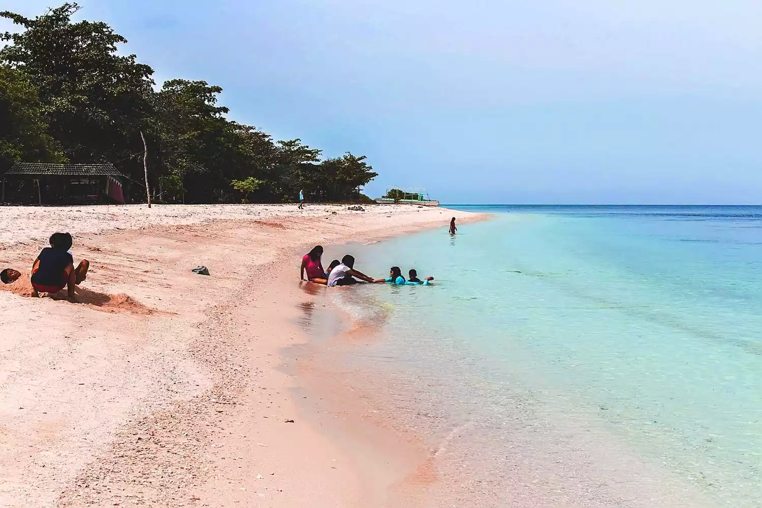 Tourists walking on the pink coralline sand of Great Santa Cruz Island in the Philippines.