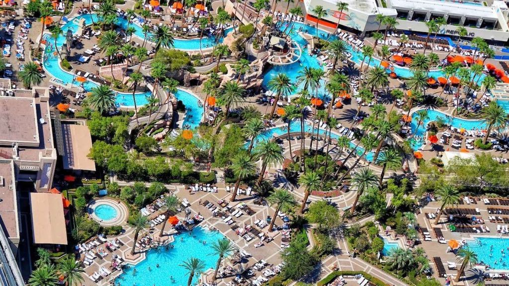 High-angle view of the Grand Pool Complex featuring waterfalls and poolside cabanas at a large hotel.