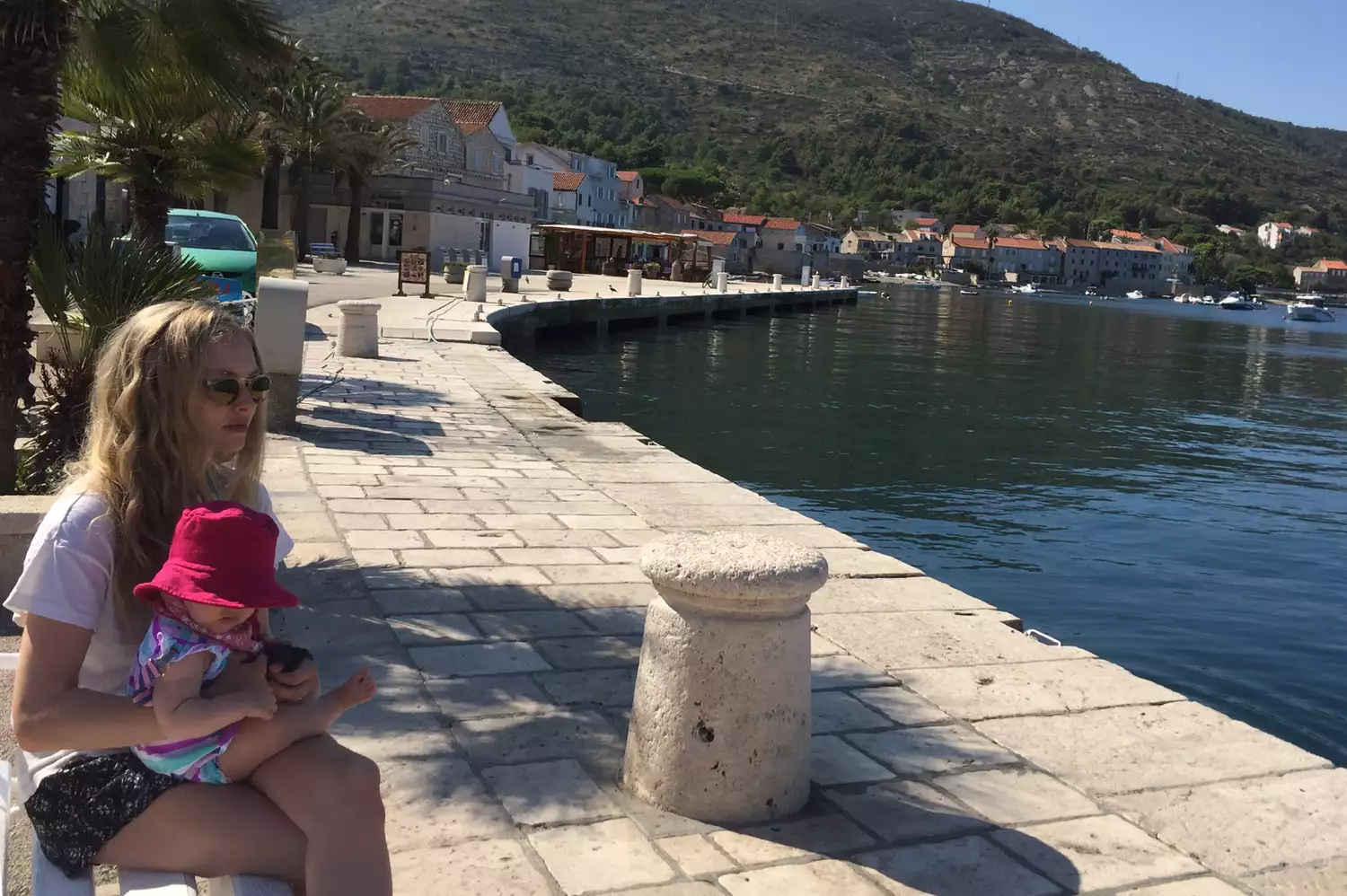 Amanda Seyfried sitting with her toddler daughter on a seaside wall in a coastal Croatian town.