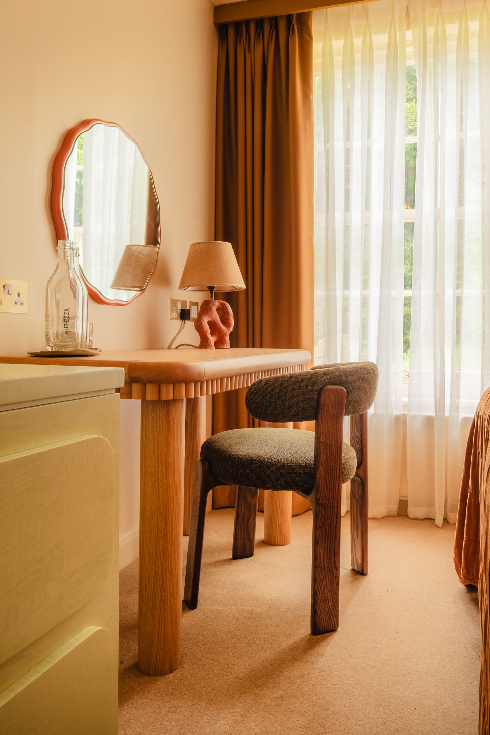A close-up of a handcrafted wooden desk and stool positioned by a window.