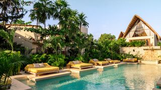 A luxury boutique hotel pool in Tulum surrounded by tropical trees and modern villa structures.