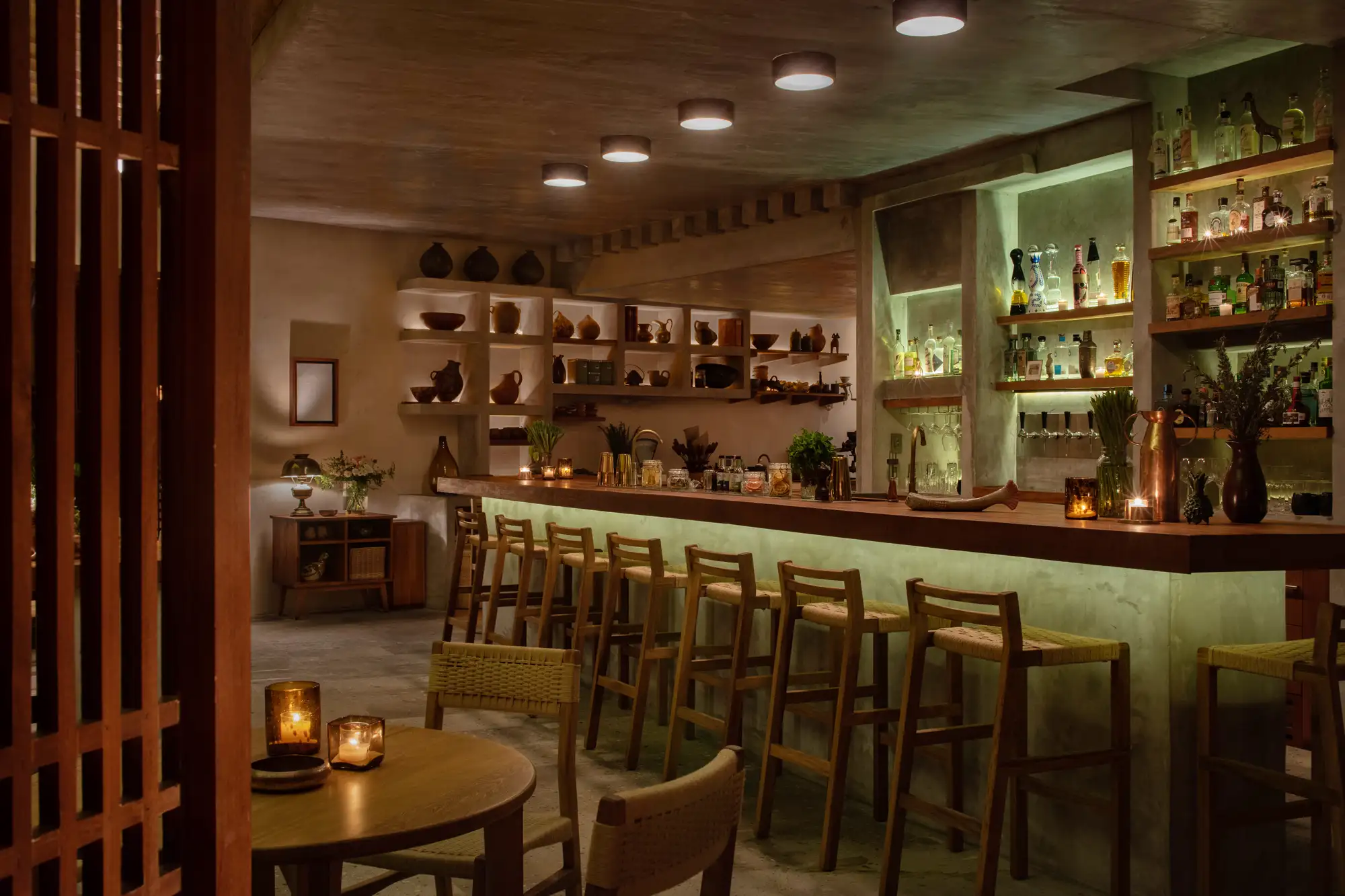 A dimly lit, sophisticated bar with high chairs and shelves of premium spirits at Zapote Bar.